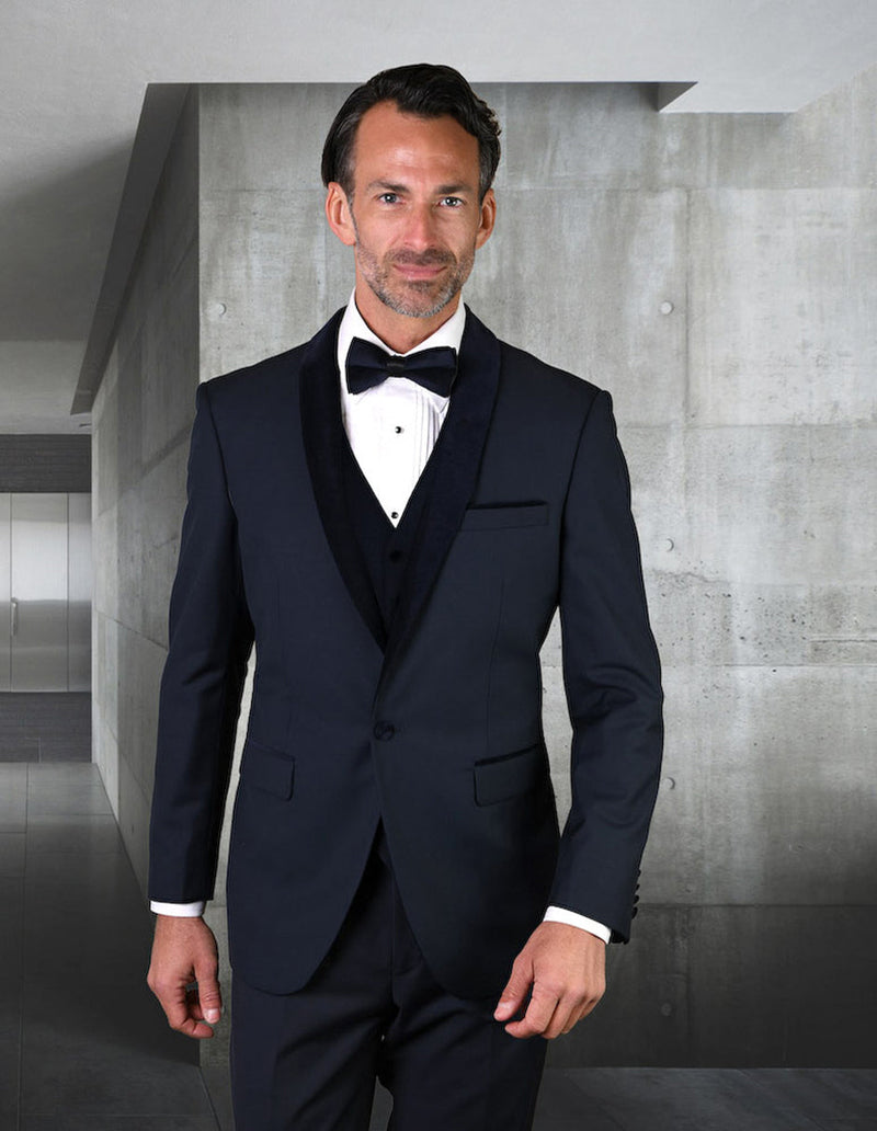 Navy wool tuxedo with velvet shawl lapel. Tailored fit jacket, single button, side pockets. Matching vest, smooth, structured material. Includes white shirt, black bow tie. Formal and elegant.
