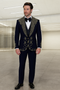 Navy tuxedo with shawl collar, gold embroidery on shoulders and front. Smooth, tailored fabric. Matching straight-cut trousers. Embellishments enhance the jacket's design.
