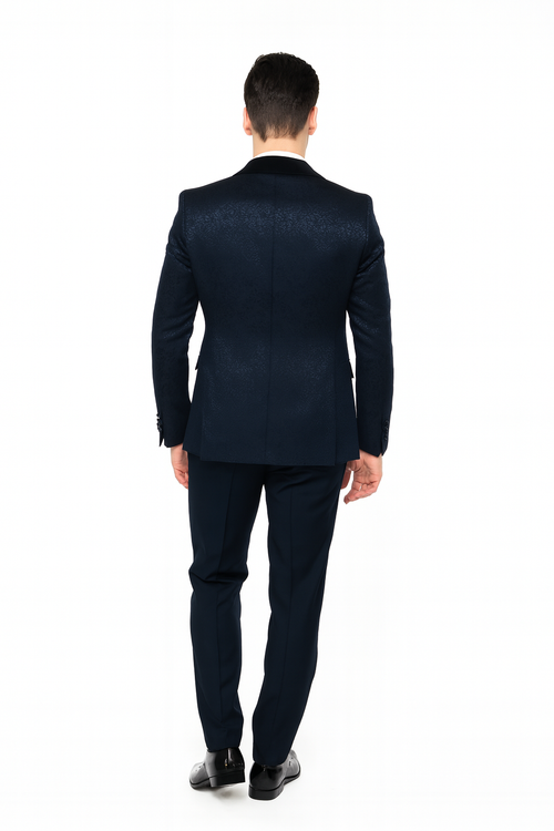 Navy jacquard tuxedo with black velvet shawl lapel. Double-breasted, fitted, textured fabric. Tailored trousers. Subtle pattern on back. Streamlined silhouette, consistent color palette emphasizing textural differences.
