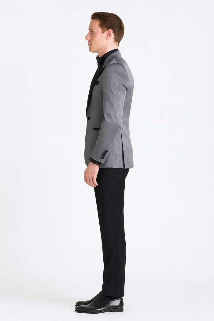 Silver metallic tuxedo suit with black satin peak lapel and tailored silhouette. Fitted form, visible buttons, and contrasting textures. Black trousers complement the design, smooth and structured materials.
