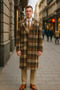 Vintage men's wool plaid overcoat. Long, straight cut with classic collar. Brown, beige, and orange plaid pattern. Features two front pockets and three-button closure. Long, tapered sleeves.
