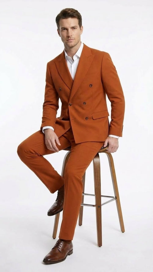 Burnt orange double-breasted suit made from a smooth fabric. The jacket features two rows of dark buttons and a notched lapel. The trousers are tailored with a slim fit.