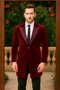 Men's burgundy velvet tuxedo with a long, tailored blazer. Features notched lapels, two pockets, and a single-button closure. Contemporary design for formal events.

