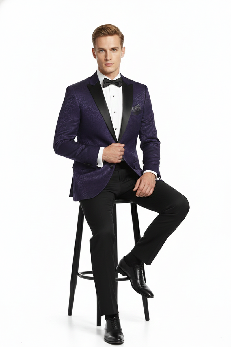 Men's purple paisley tuxedo jacket: structured, single-button closure, peaked lapels. Glossy fabric with purple paisley. Black trousers create contrast, black lapel accents.
