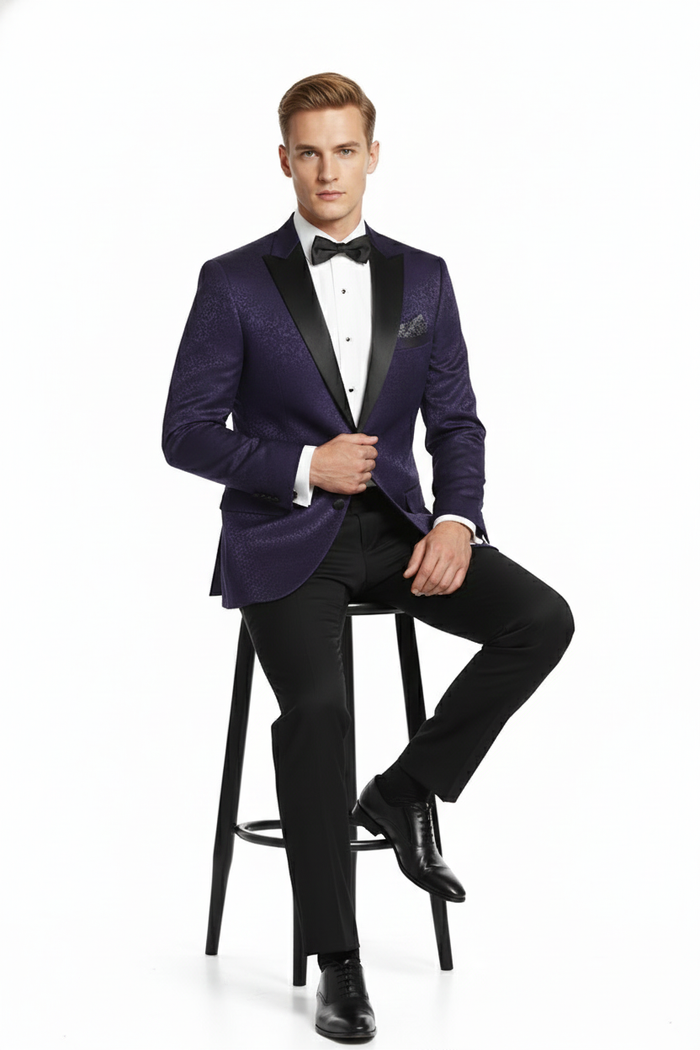 Men's purple paisley tuxedo jacket: structured, single-button closure, peaked lapels. Glossy fabric with purple paisley. Black trousers create contrast, black lapel accents.
