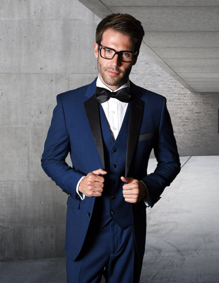 Sapphire blue modern fit wool tuxedo. Two-button jacket with satin lapels, matching vest, and structured fit. Includes black bow tie and white dress shirt.
