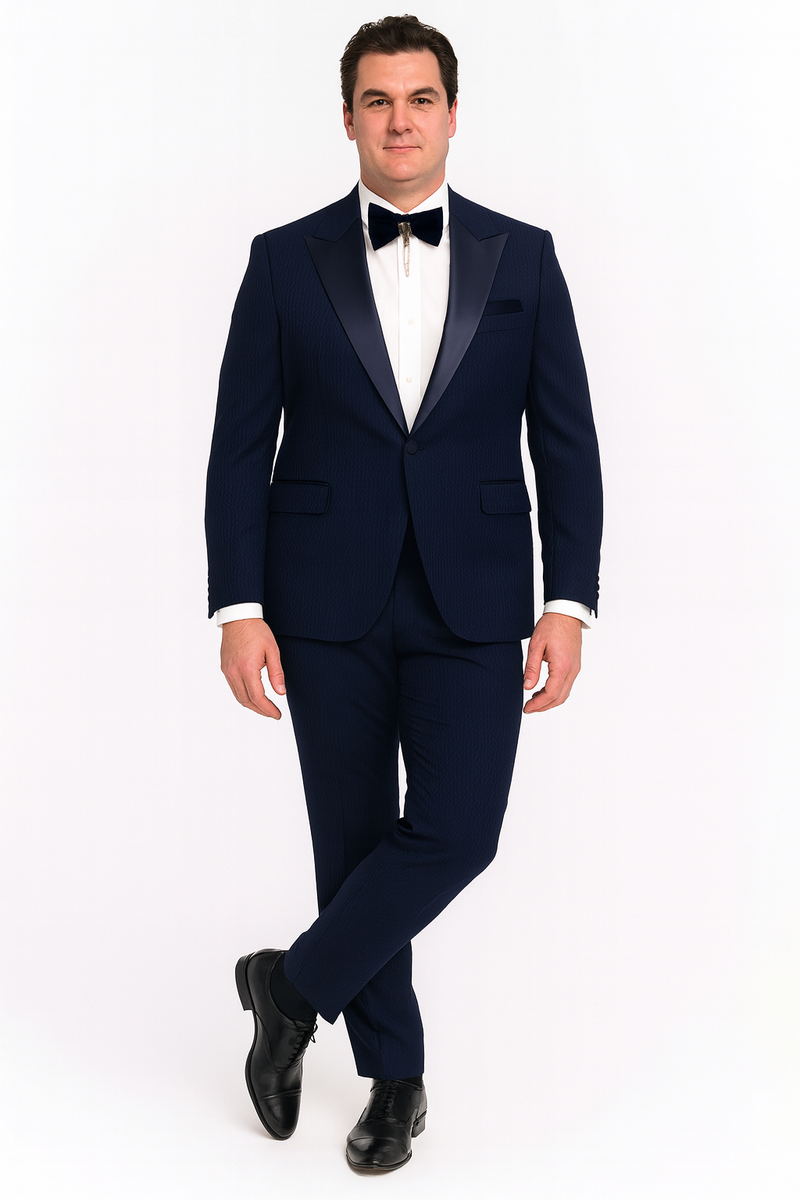 Navy blue tuxedo with satin peak lapel, structured shoulders, and matching trousers. Textured fabric. Includes white shirt, black bow tie. Classic formal wear.
