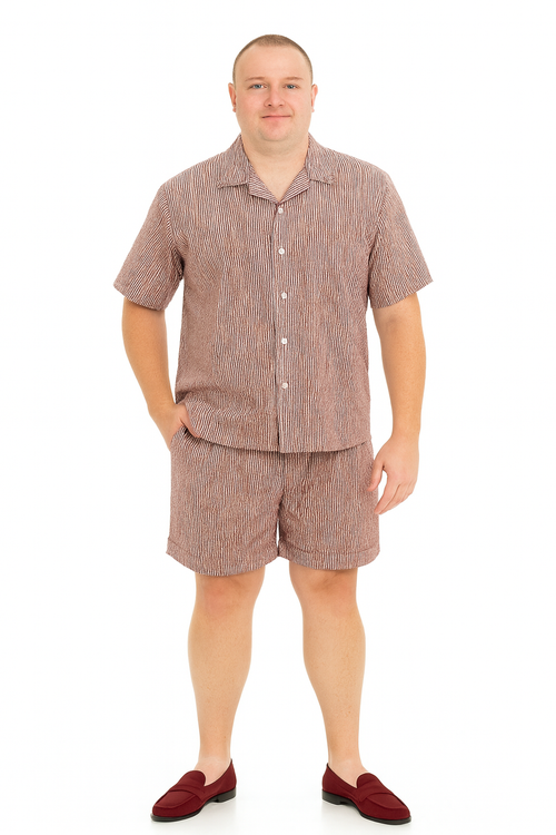 Burgundy seersucker short set: button-up shirt with collar, short sleeves, and matching shorts. Textured, striped fabric in burgundy and lighter hues. Relaxed fit; shirt at waist, shorts above knee.
