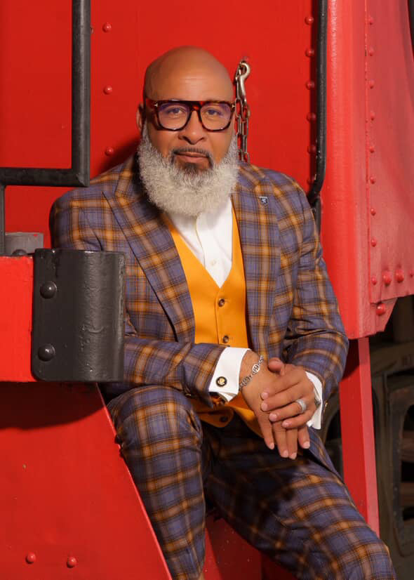 Stacy Adams men's grey-gold windowpane plaid suit. Fitted silhouette, structured shoulders. Includes vest. Jacket: notched lapels, flap pockets. Tapered leg pants. Bold plaid design.

