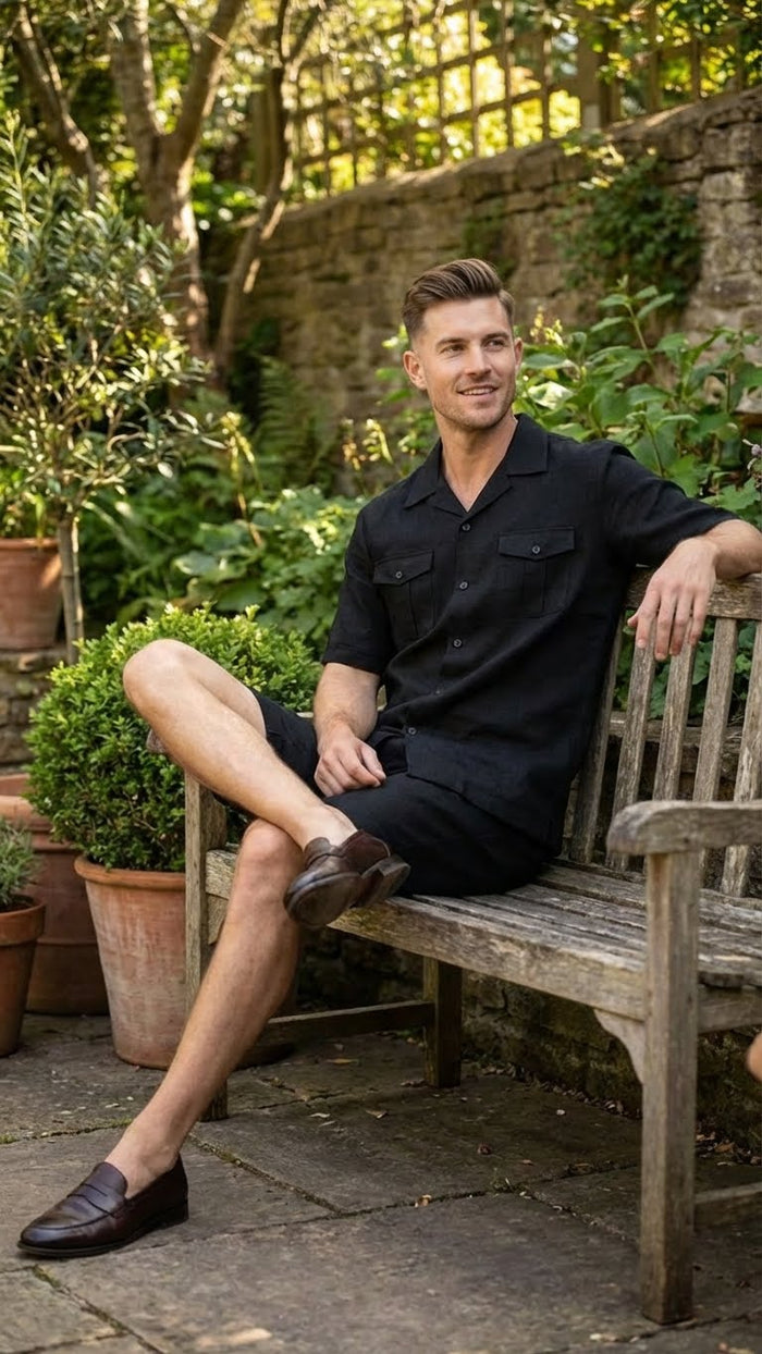 Men’s black walking suit features a short-sleeve button-up shirt with a collar and two front pockets, paired with knee-length shorts. The fabric appears to be lightweight, and both the shirt and shorts are uniform in color and style, creating a cohesive look.