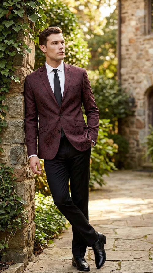 Men's burgundy velvet paisley blazer sport coat. Tailored fit, single-button closure, notched lapels. Features a patterned design with floral accents. Paired with a black tie and pants for a formal look.
