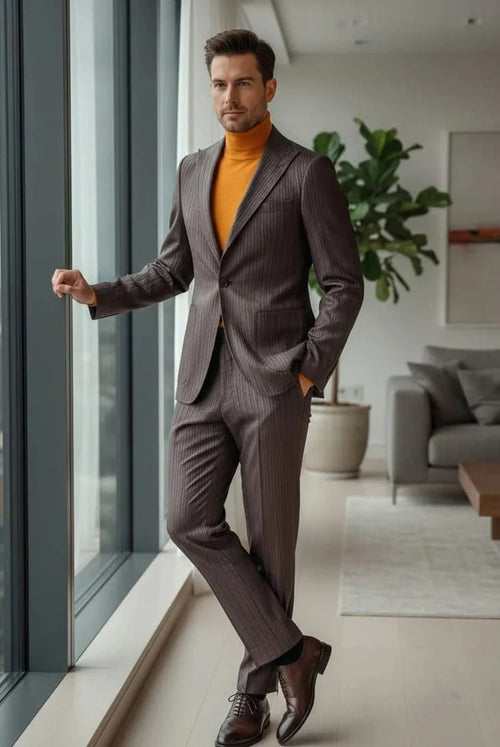 Brown, slim fit men's suit with subtle pinstripes. Features a one-button peak lapel jacket and slim trousers. Woven fabric for a structured look. Paired with an orange turtleneck.
