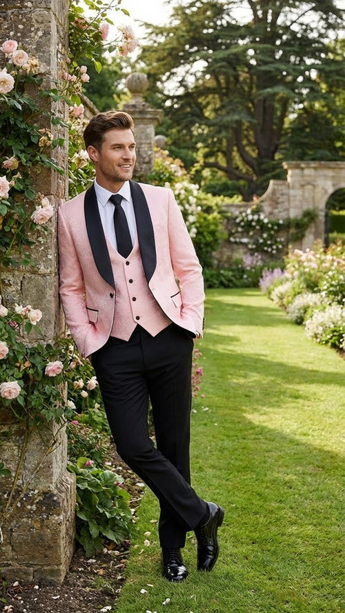 Men's tuxedo suit set: blush pink jacket (black shawl lapel, tailored fit), matching waistcoat, and black straight-leg trousers. Black pocket details.
