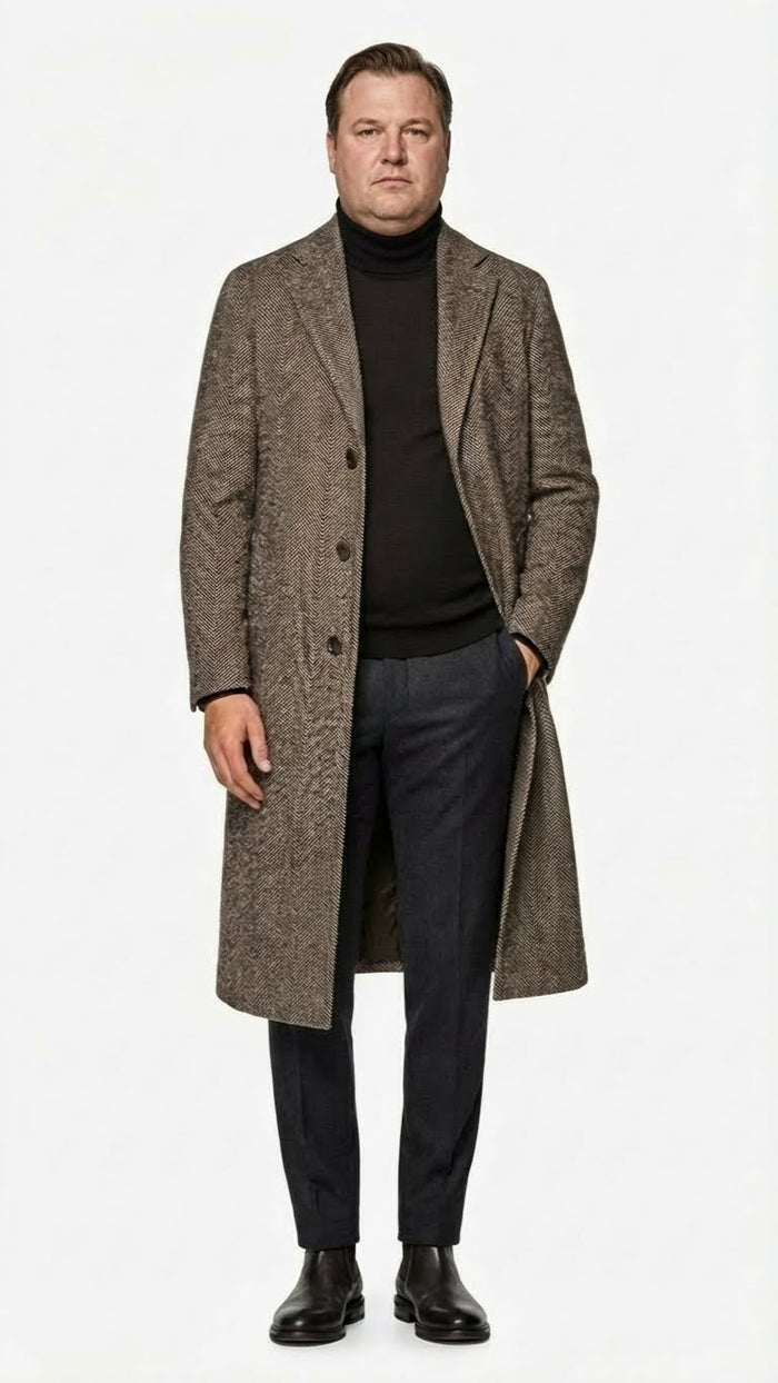 Men's overcoat in black-grey herringbone tweed wool blend. Long, straight cut with two front buttons and side pockets. Textured pattern, back vent for movement.
