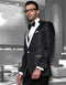 Black men's tuxedo with swirling pattern and notch lapel. Glossy fabric, tailored fit, white accents (pocket square, lapel trim).
