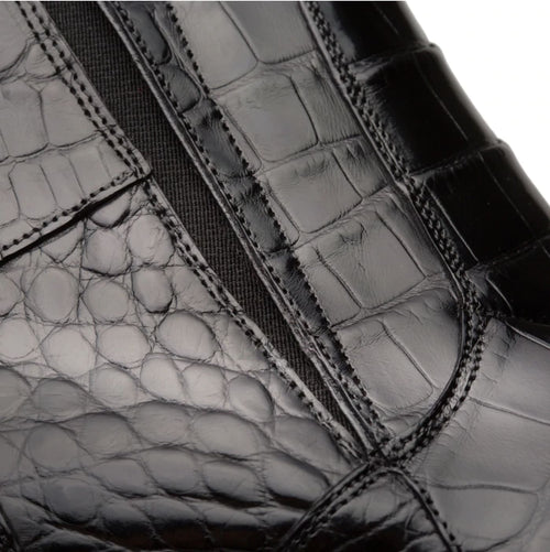 Black Belucci alligator zipper boot: sleek pointed-toe, ankle-height silhouette. Shiny black alligator leather upper with visible scales and glossy finish. Elastic side panels for comfort. Inner zipper for easy wear.
