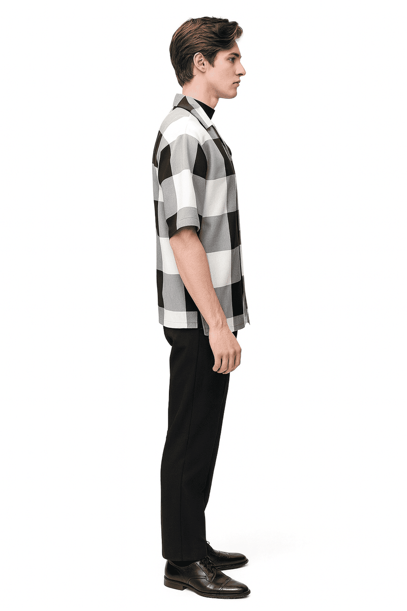 Men's black & white checkered short sleeve shirt (loose fit, button-up) with black straight-leg pants. Casual outfit, large checker pattern, flat collar, and smooth fabric.
