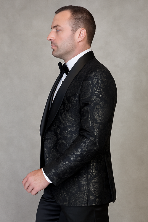 Men's black paisley tuxedo. Tailored single-breasted jacket with paisley lace print and satin shawl collar. Fitted waist and long sleeves. Paired with black dress trousers for a modern, cohesive look.
