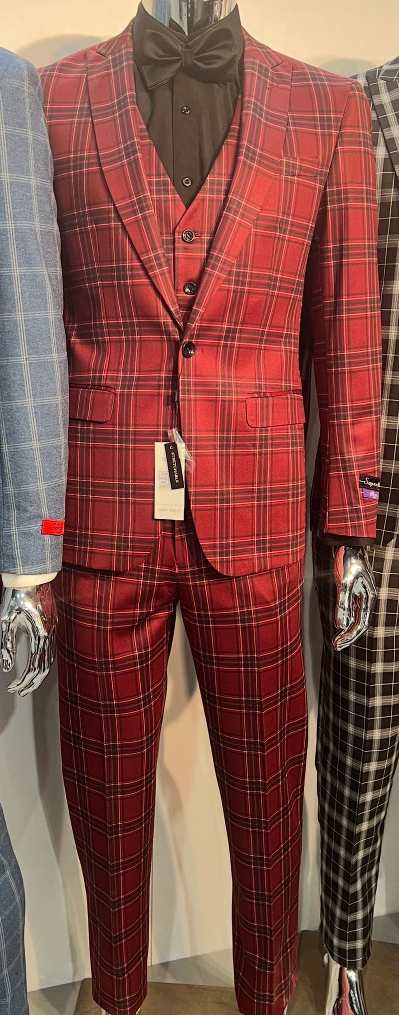 Burgundy plaid three-piece suit: fitted blazer (peaked lapel, two buttons), matching slim-fit trousers, and vest. Burgundy with black/red plaid. Includes a black bow tie and button-up shirt.
