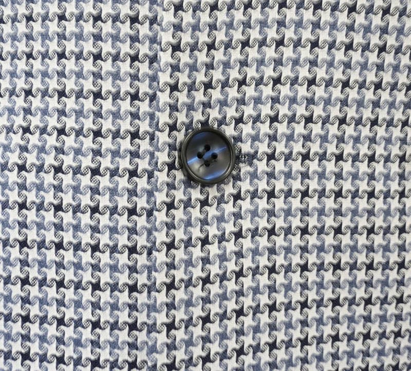 Blue houndstooth double-breasted jacket with a light/dark blue pattern. Features a black, four-hole button detail centered on the fabric.
