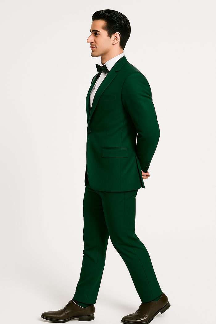 Emerald green tuxedo set. Fitted blazer, notched lapel, single button. Slim-fit trousers. Textured, uniform fabric. White shirt and black bow tie complete the look.
