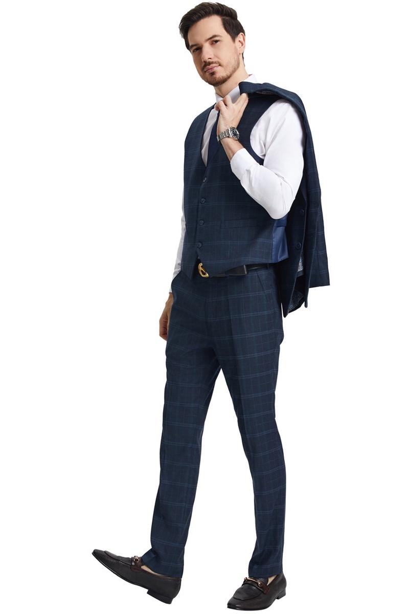 The men's Stacy Adams vested modern fit suit features a navy blue windowpane plaid pattern with a fitted shape. It includes a vest with a button closure, matching trousers, and a stylish blazer draped over one shoulder.