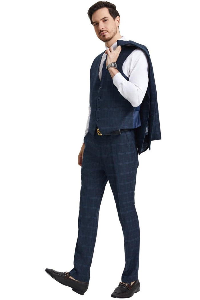 The men's Stacy Adams vested modern fit suit features a navy blue windowpane plaid pattern with a fitted shape. It includes a vest with a button closure, matching trousers, and a stylish blazer draped over one shoulder.
