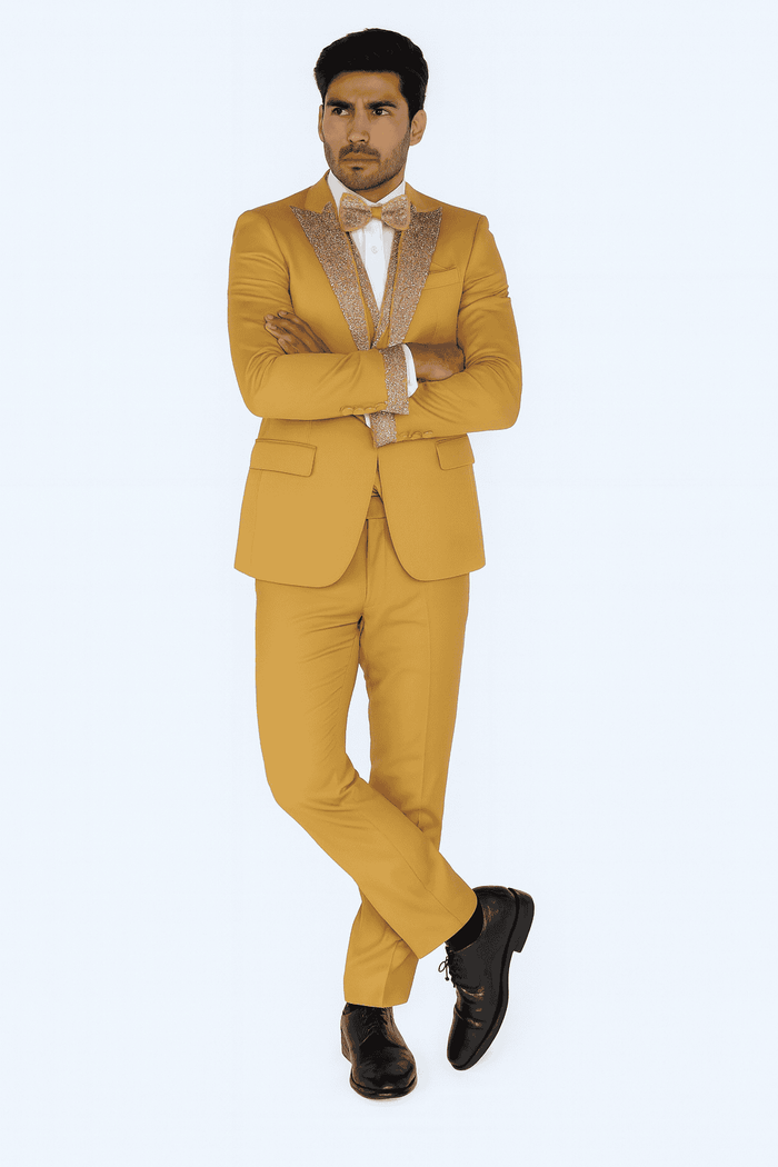 Champagne gold men's prom tuxedo: fitted jacket with glitter lapels, matching trousers, white shirt, and bow tie. Completed with black dress shoes.
