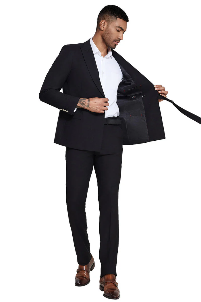 Men's black, slim-fit suit. French front, peak lapel jacket with a structured design and strap detail. Slim pants. Smooth, tailored material with a visible inner lining when the jacket is open.
