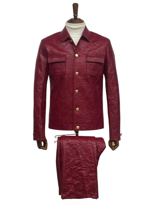 Burgundy two-piece faux leather suit. Slim fit, crinkled texture. Collared jacket with chest pockets & decorative buttons, matching trousers. Casual style.
