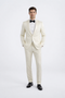 Ivory peak lapel slim fit tuxedo: single-breasted, 2-button closure. Satin-like finish jacket with matching trousers. Includes white dress shirt and black bow tie.