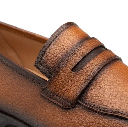 Men's cognac deerskin penny loafers with rounded toe and low profile. Textured, glossy upper. Classic penny keeper strap. Smooth, contrasting interior lining.
