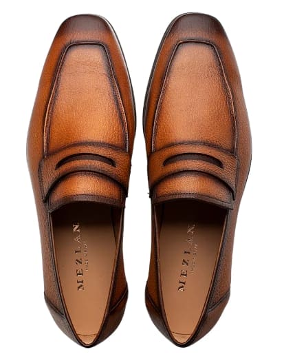 Mezlan men's cognac deerskin penny loafers: smooth, rounded, stitched upper, penny slot. Rich brown color, natural texture. Light tan interior. Flat heel, sleek silhouette, elegant.
