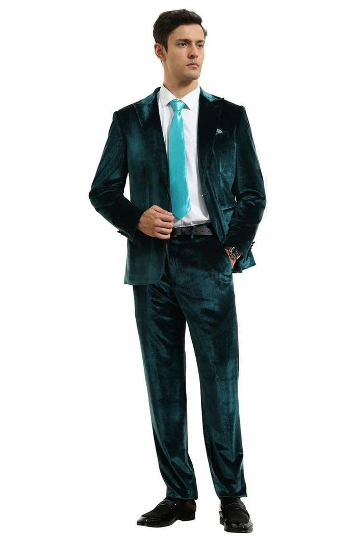 Slim-fit teal green velvet men's suit. Single-breasted jacket, peaked lapels, and matching trousers. Smooth, glossy texture. Includes a light blue tie.
