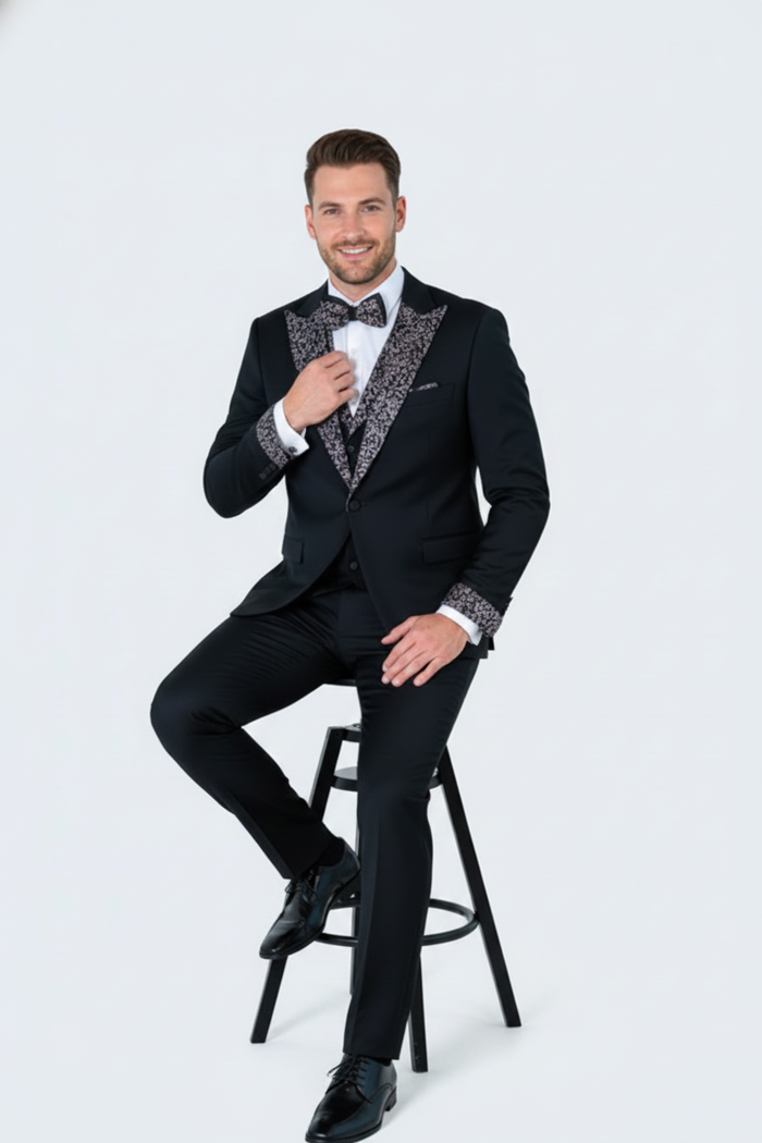 Men's black tuxedo with a fitted cut. It has a white, embellished shawl collar and cuffs. The fabric is shiny, smooth, and patterned.
