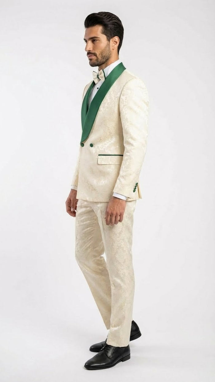 Ivory tuxedo suit with emerald green accents. Jacquard pattern, shawl collar, and two-button closure on jacket. Tailored ivory pants. Green pocket square. Black dress shoes complete the formal look.
