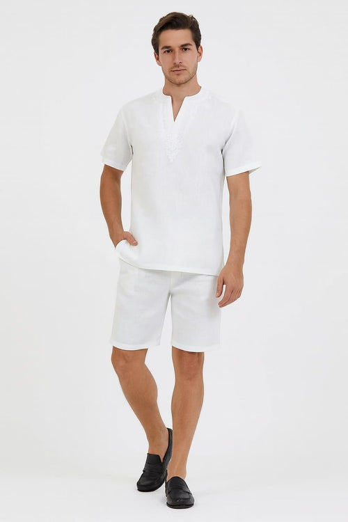 Men's white short set. V-neck shirt with short sleeves and matching shorts, both lightweight with subtle embroidery. Relaxed fit shorts end above the knee with folded hem.
