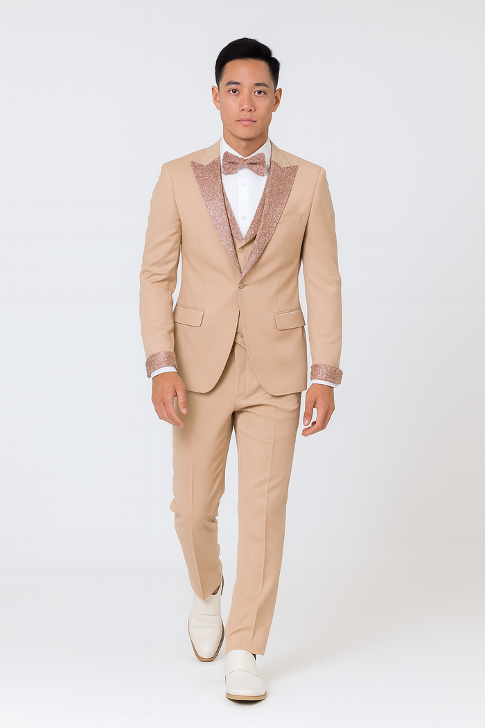 Men's champagne rose gold prom tuxedo: tailored jacket w/ rose gold glitter lapel, matching trousers. Single-button jacket, white shirt, rose gold bow tie. White footwear contrasts the champagne ensemble.
