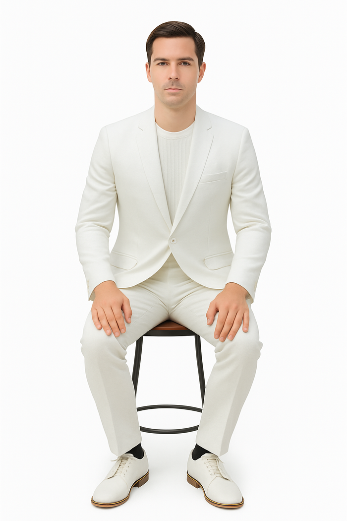 Men's cream linen suit: relaxed hybrid fit, no collar. Fitted blazer, single button, one pocket. Straight-leg trousers. Breathable linen. Worn with matching top, white shoes, black socks.
