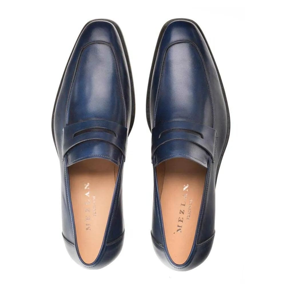 Navy burnished calfskin penny loafer by Mezlan. Sleek, streamlined shape with a rounded toe and penny slot detail. Smooth navy leather upper. Flat, elongated sole. Neutral interior lining.
