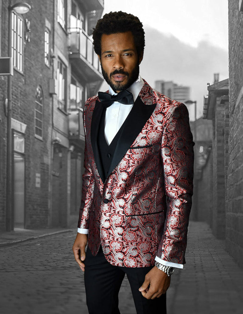 Red floral one-button tuxedo with peak lapel. Features a shiny, textured pattern, tailored sleeves with white cuffs, and a black vest. Paired with black trousers.
