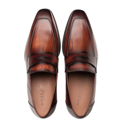 Mezlan men's penny loafers in cognac rust. Leather construction with a glossy finish and gradient color. Rounded toe, penny slot, and flat heel. Smooth inner lining.
