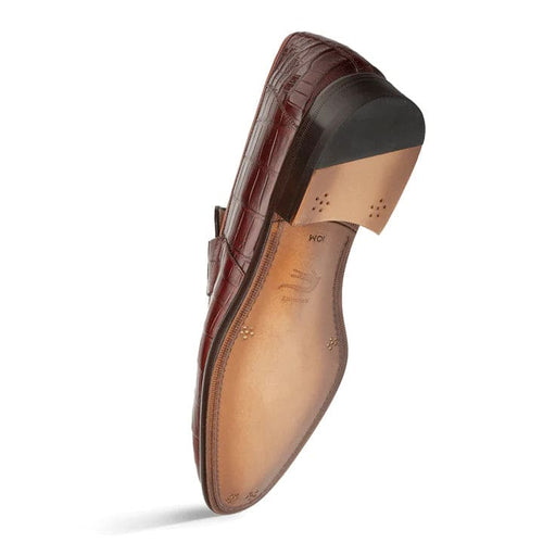 Mezlan Piccolo Sport Tan penny loafer crafted from glossy, textured alligator leather. Features a structured silhouette, flat heel, and leather/rubber sole. Interior boasts smooth tan leather lining.
