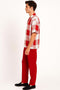 Men's red & white checkered short-sleeve shirt (relaxed fit, camp collar) with pocket, worn with solid red tailored pants.
