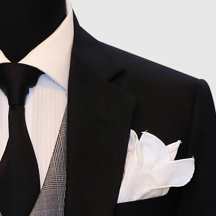 Black suit jacket paired with a gray plaid vest. The jacket has a structured form and is complemented by a white dress shirt and a black tie. A silk white pocket square is visible in the jacket's breast pocket. The vest displays a checkered pattern in various shades of gray.
