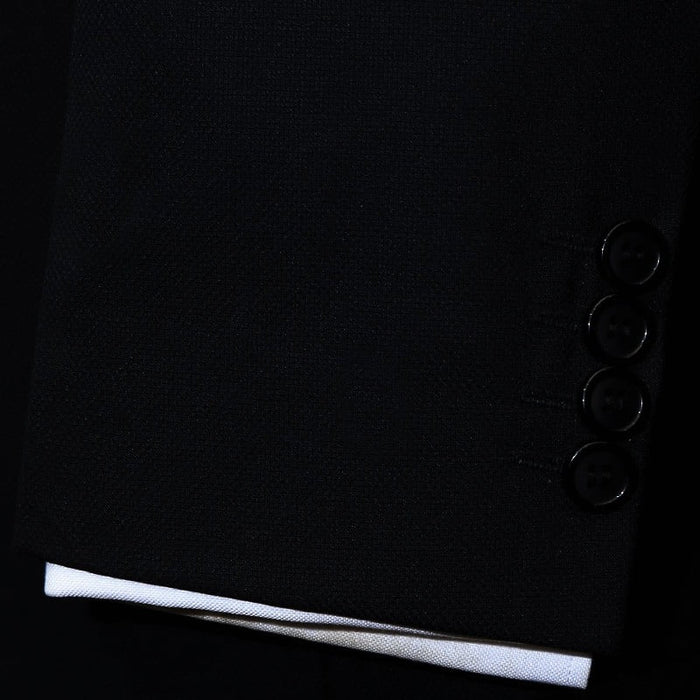 Black suit jacket featuring a cuff with five black buttons. The cuff is accompanied by a white shirt sleeve peeking out at the end, contrasting with the dark fabric of the suit. The overall appearance is sleek and tailored.