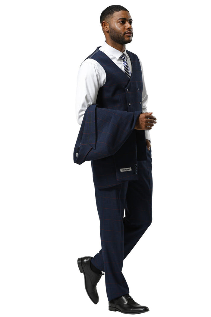 Navy glen plaid Stacy Adams suit with a one-button peak lapel. Features a double-breasted vest and tailored trousers. Includes a textured fabric, with a dress shirt and patterned tie visible. Jacket held over the arm.

