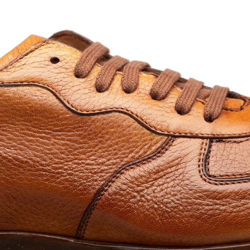Mezlan's Gerardo men's sneakers. Cognac deerskin upper with a smooth, textured finish. Rounded toe, subtle seam detailing, and brown laces. Contrasting leather panel.
