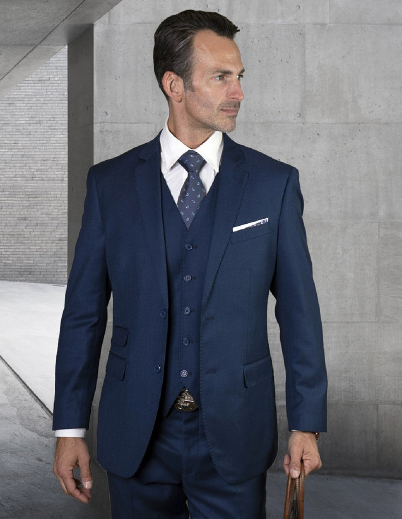 Modern fit, sapphire blue men's suit. Features a 2-button blazer, vest, & straight-leg trousers. Solid weave with pick stitch detail. Includes a breast pocket with a white pocket square. Worn with a white shirt and patterned tie.