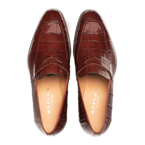 Mezlan men's penny loafers crafted from dark brown American alligator. Sleek design with rounded toe, penny strap, and textured alligator skin. Tan leather lining, minimalistic style.
